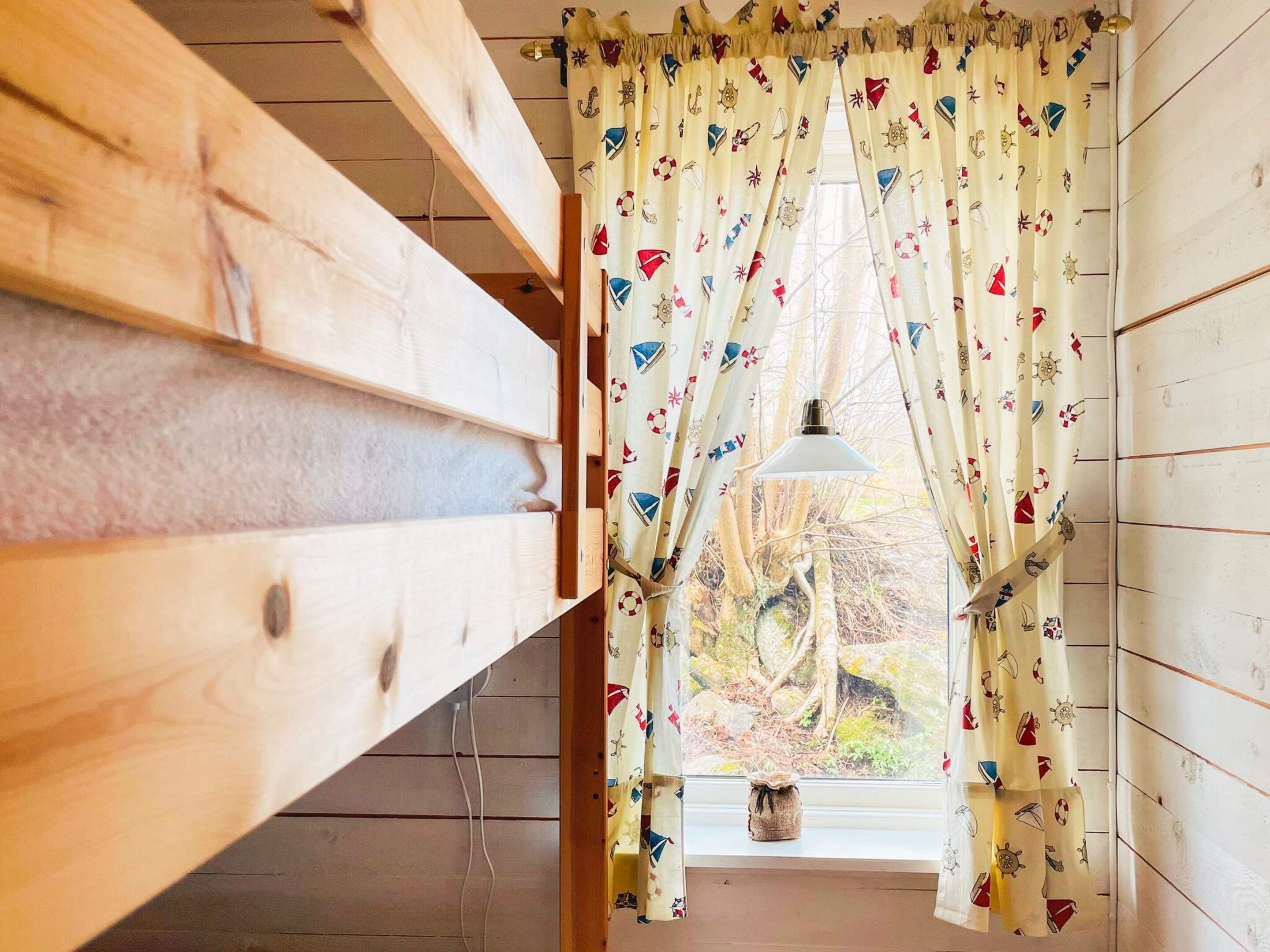 A room with a wooden slat ceiling, a window with a curtain featuring nautical patterns, and a hanging lamp.