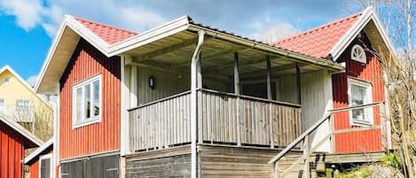 A red wooden house with a porch and a staircase leading to a second floor.