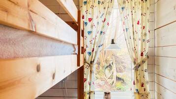 A room with wooden walls, a window with a curtain featuring nautical designs, and a hanging lamp.
