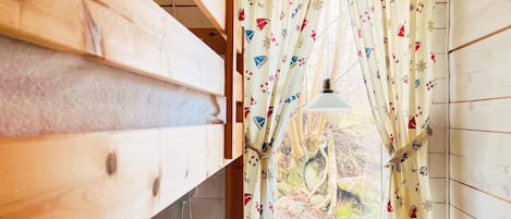 A room with wooden walls, a window with a curtain featuring nautical designs, and a hanging lamp.