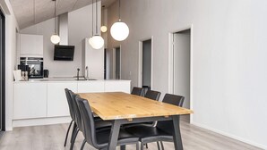 Et moderne køkken med en central ø, et spiseområde med et træbord og sorte stole, samt hængende lamper.