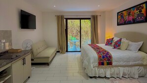 Una habitación de hotel moderna con cama, sofá, televisión y balcón con vistas a zonas verdes.
