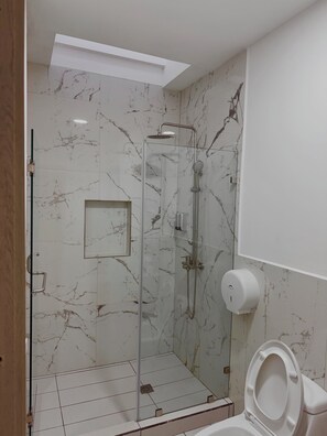 Egy modern fürőszoba üvegfallal elválasztott zuhanyzóval, WC-vel és márványmintás falakkal.