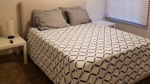 A bedroom with a bed, a nightstand, a ceiling fan, and a window with blinds.
