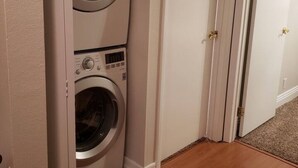 A laundry room with two stacked washers and dryers, a wooden floor, and white walls.