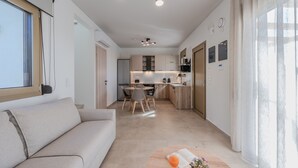 A modern living room with a sofa, a dining table with chairs, and a kitchen in the background. - Meli & Gio 1 villa,private pool, near tavern,Rethymno (Viran Episkopi)