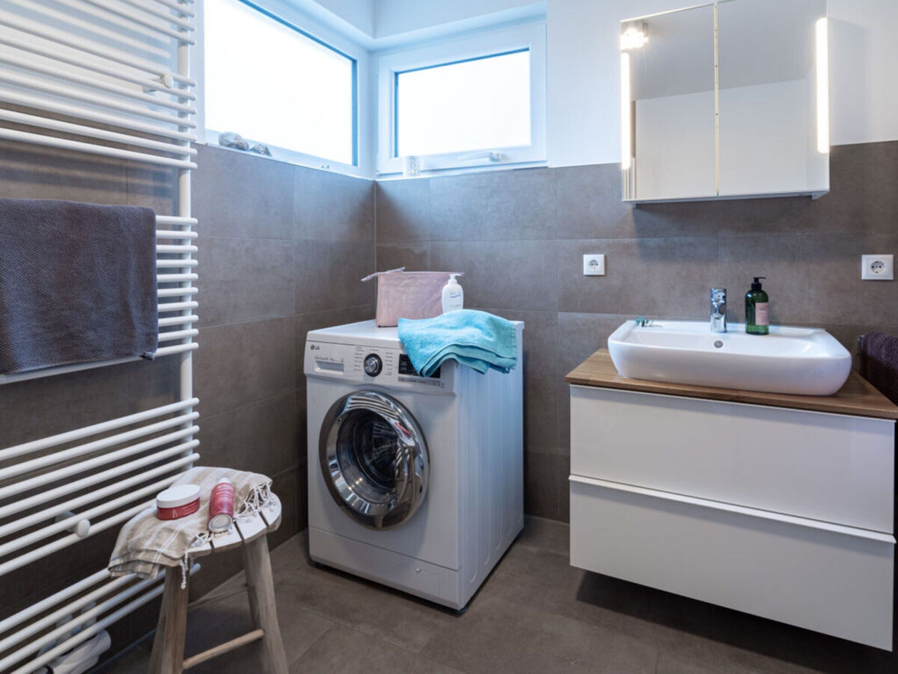 A compact bathroom with a washing machine, a sink, and a small table with toiletries.