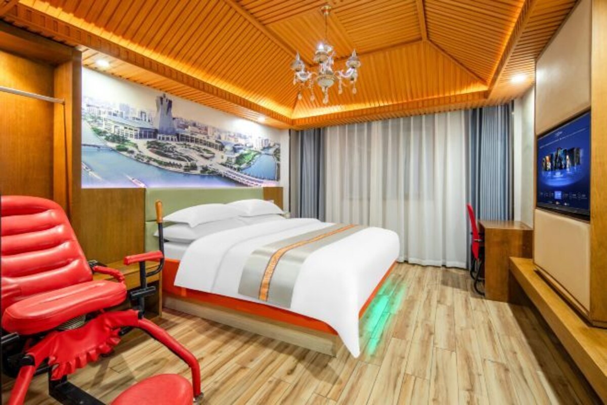 A hotel room with a bed, a red chair, a TV, and a wooden ceiling.