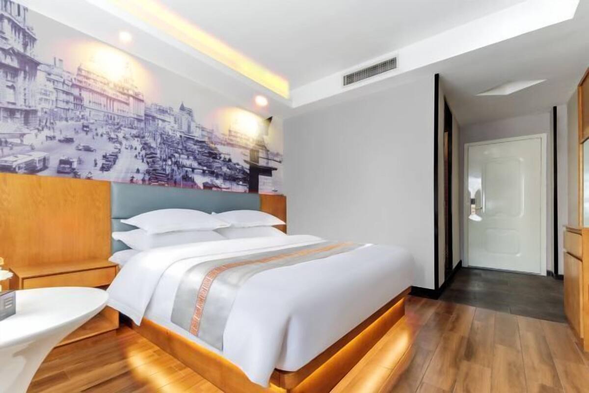 A hotel room with a large bed, a bedside table, a wall-mounted TV, and a cityscape mural.