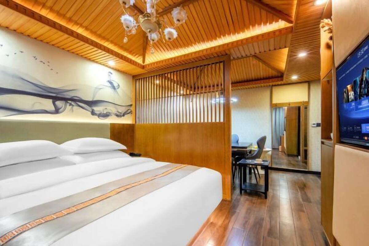 A modern hotel room with a large bed, wooden ceiling, and a wall-mounted TV.