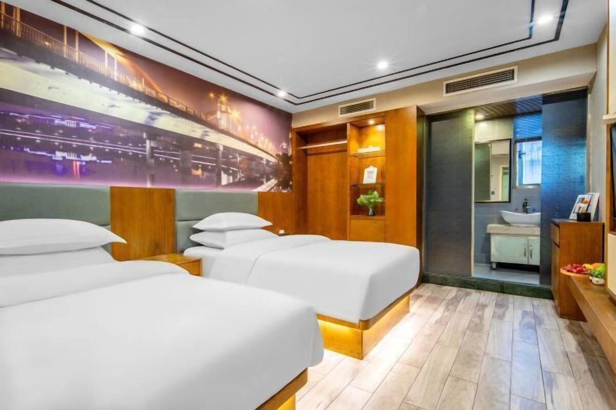 A hotel room with two beds, a large wall mural, a wooden cabinet, and a bathroom visible through an open door.
