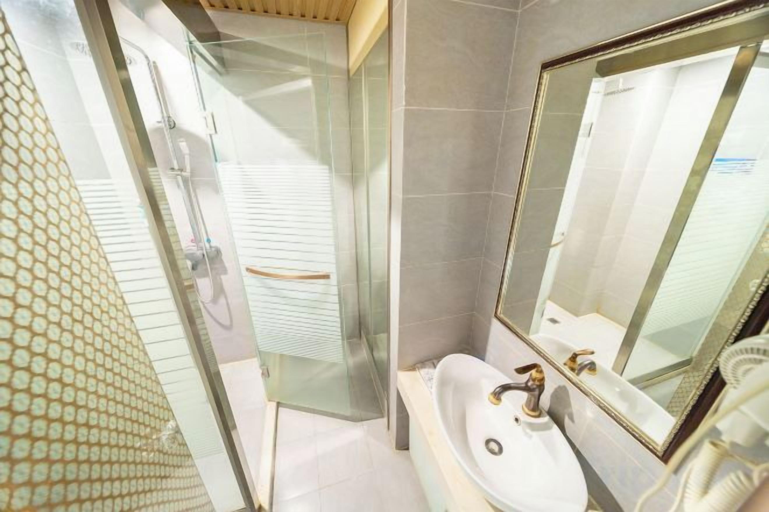 A bathroom with a glass shower enclosure, a sink with a mirror, and a tiled floor.