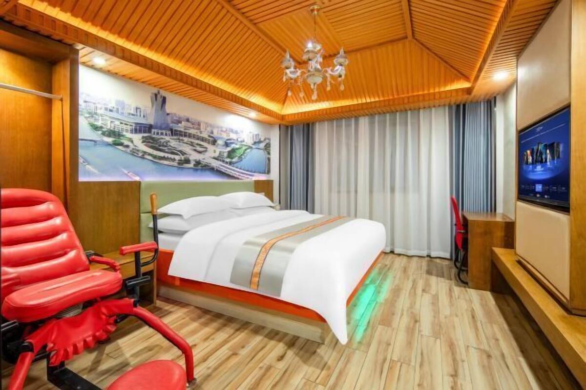 A hotel room with a bed, a red chair, a TV, and a wooden ceiling.