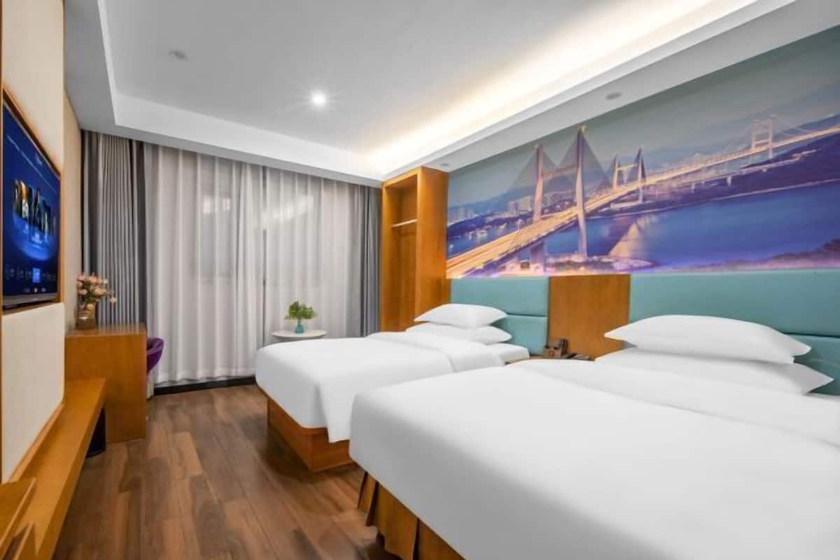 A hotel room with two beds, a TV, a small table with a plant, and a mural of a bridge.
