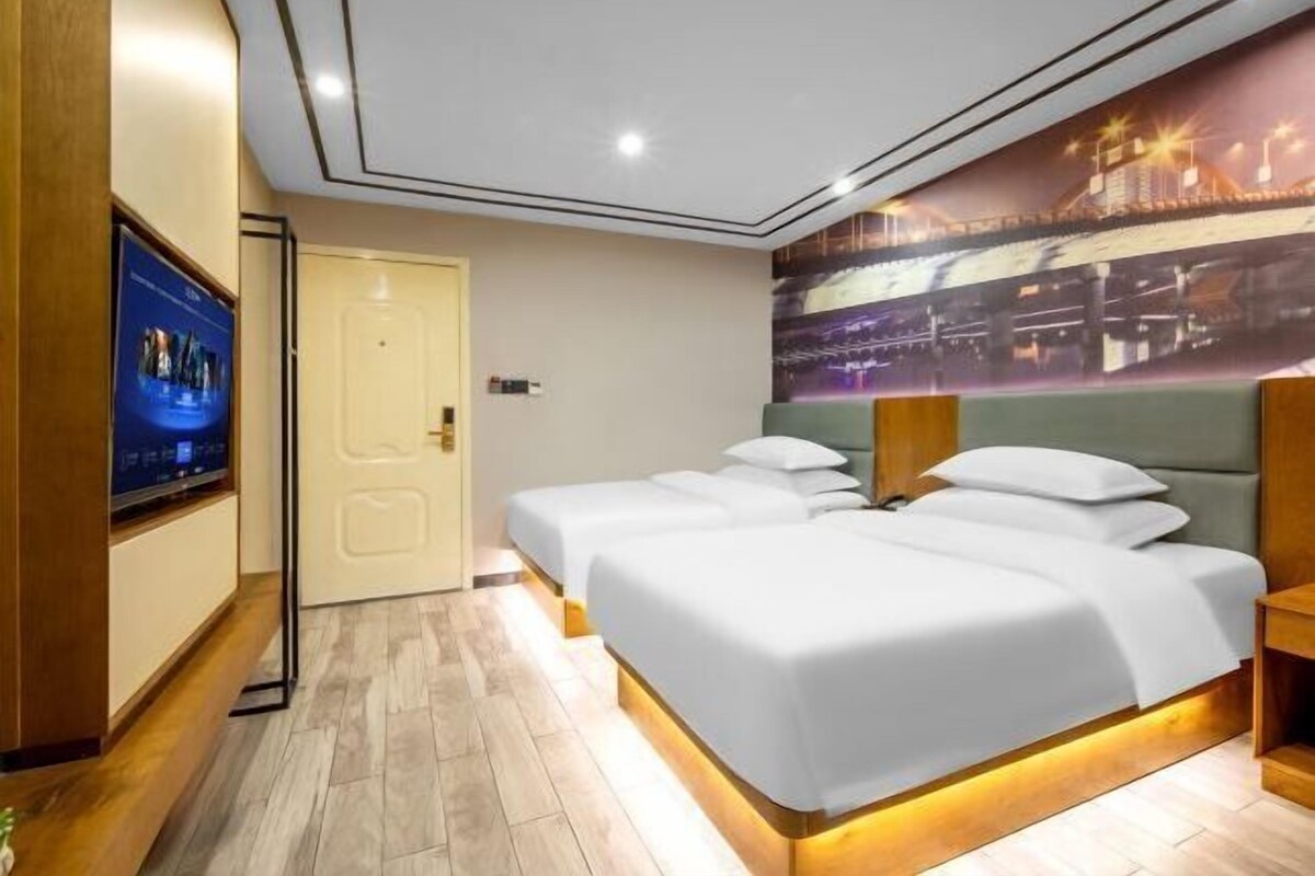 A hotel room with two beds, a television, and a mural of a cityscape.