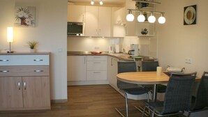 Une cuisine moderne avec des meubles blancs, une table à manger en bois et un lustre.