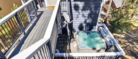 A hot tub on a wooden deck with a metal railing, surrounded by trees and a fence.