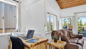 A room with a wooden ceiling, a brown leather sofa, a wooden table with a laptop, a lamp, and a small potted plant. - Mountain Palette by Avantstay Hot Tub, Game Room, Deck, Sweeping Views! (Big Bear City)