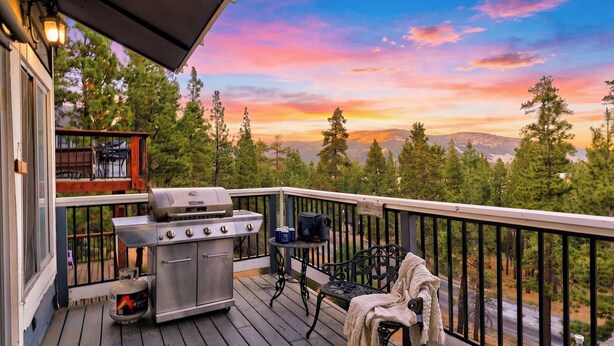 A deck with a grill, outdoor seating, and a scenic view of trees and mountains. - Mountain Palette by Avantstay Hot Tub, Game Room, Deck, Sweeping Views! (Big Bear City)