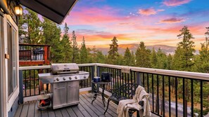 Um terraço com churrasqueira, área de estar externa e uma vista panorâmica de árvores e montanhas.