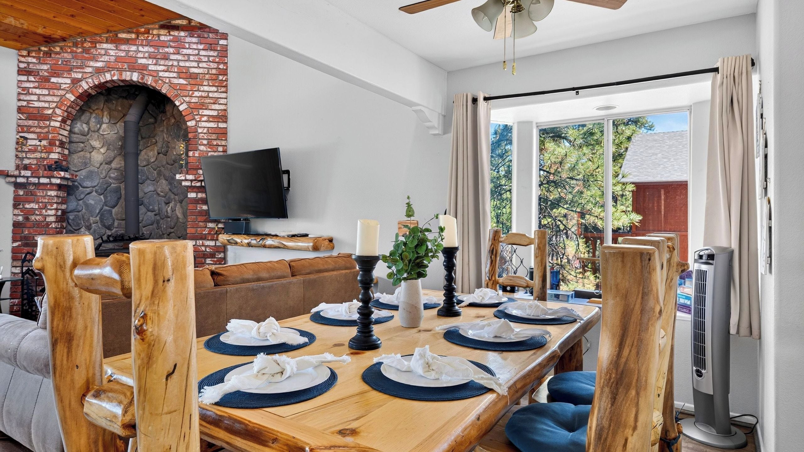 A dining area with a brick fireplace, a flat-screen TV, and a view of the outdoors.
