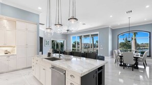 A modern kitchen with a marble island, white cabinetry, and pendant lighting.