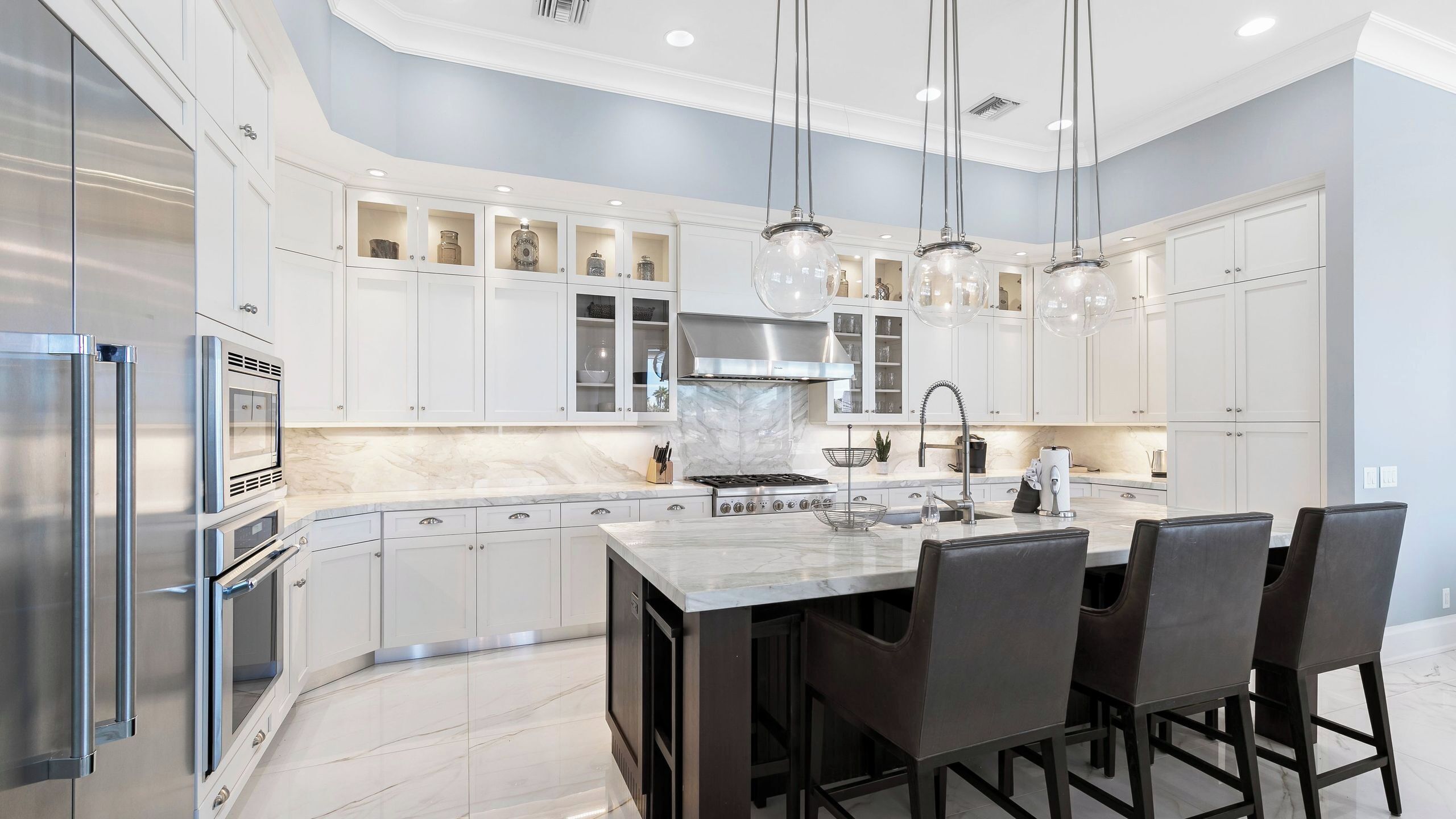 A modern kitchen with white cabinetry, a marble countertop, stainless steel appliances, and a central island with bar stools.