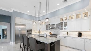 A modern kitchen with a marble island, stainless steel appliances, and pendant lighting.