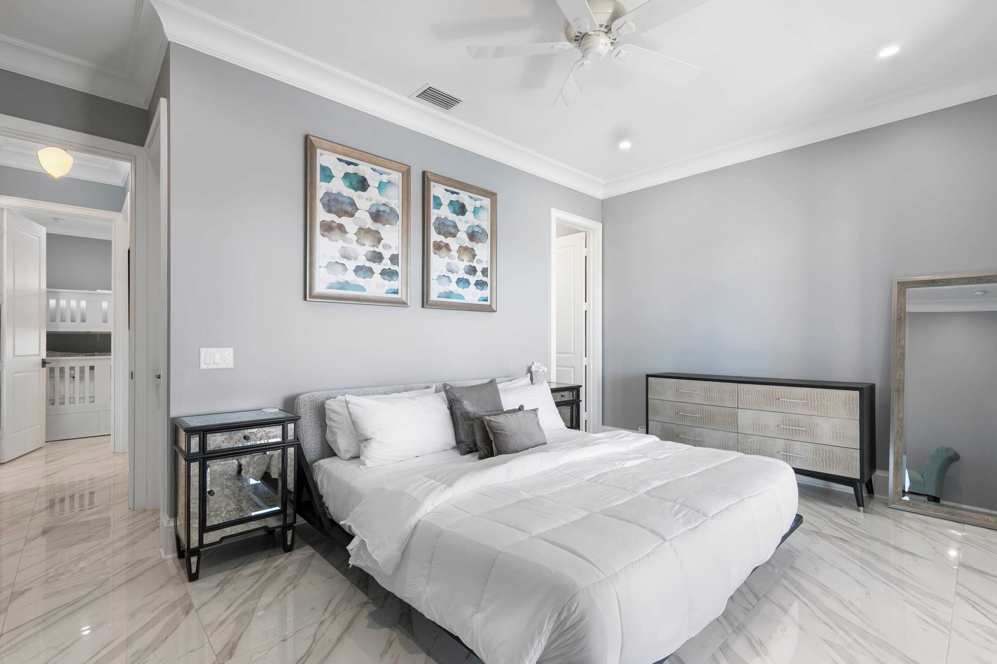 Une chambre à coucher avec un grand lit, une table de chevet, une commode et deux œuvres d’art encadrées accrochées au mur.