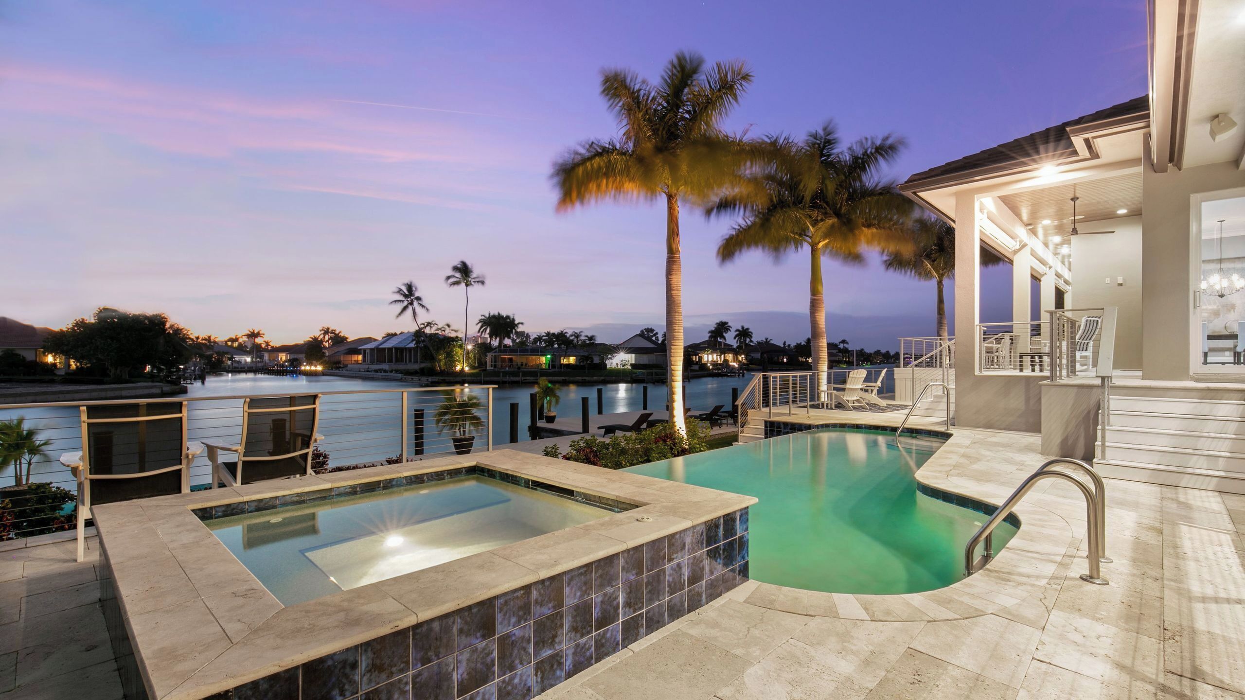 A pool area with a hot tub, lounge chairs, and palm trees.