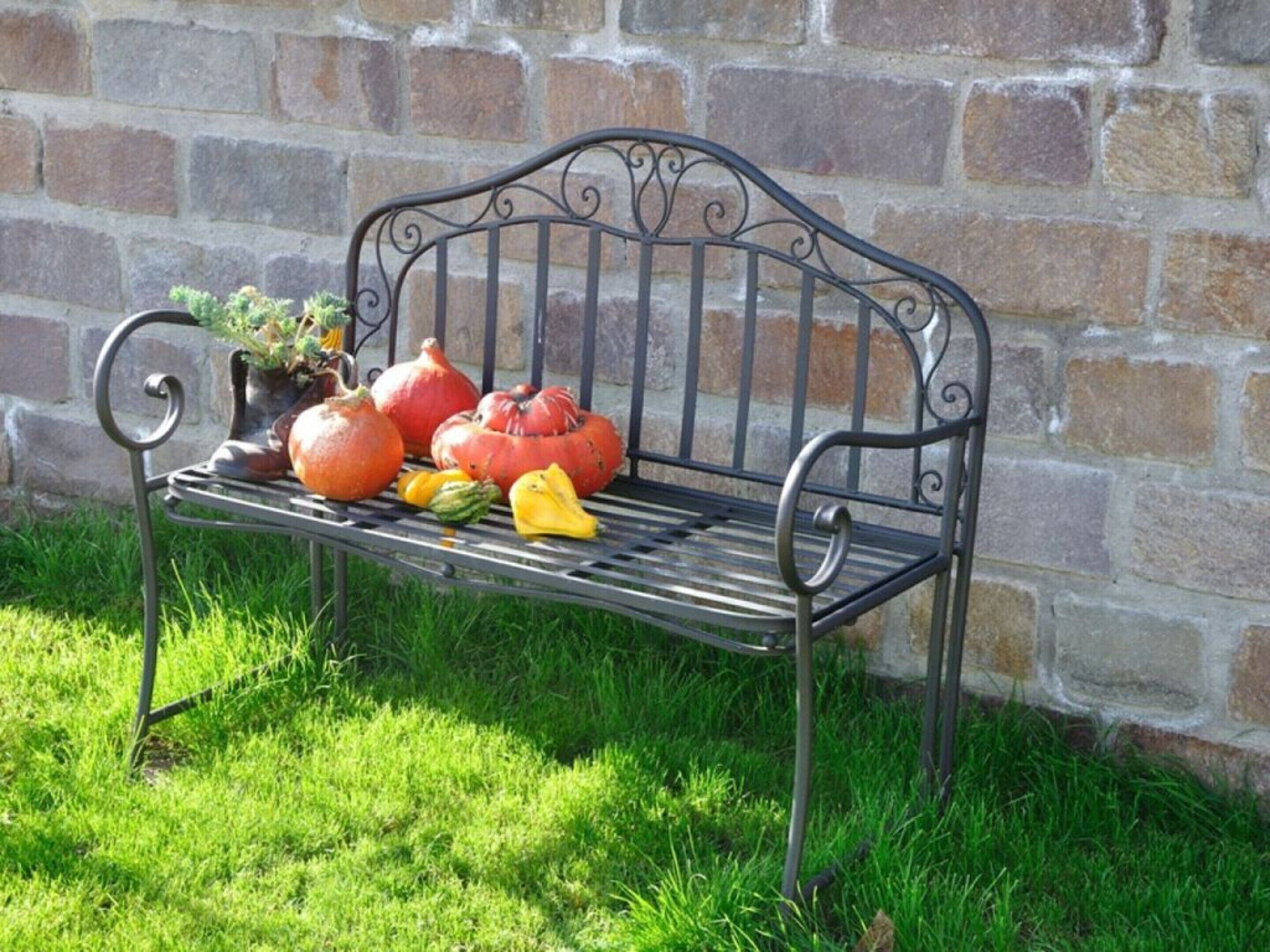 A metal bench with a potted plant and pumpkins on it.