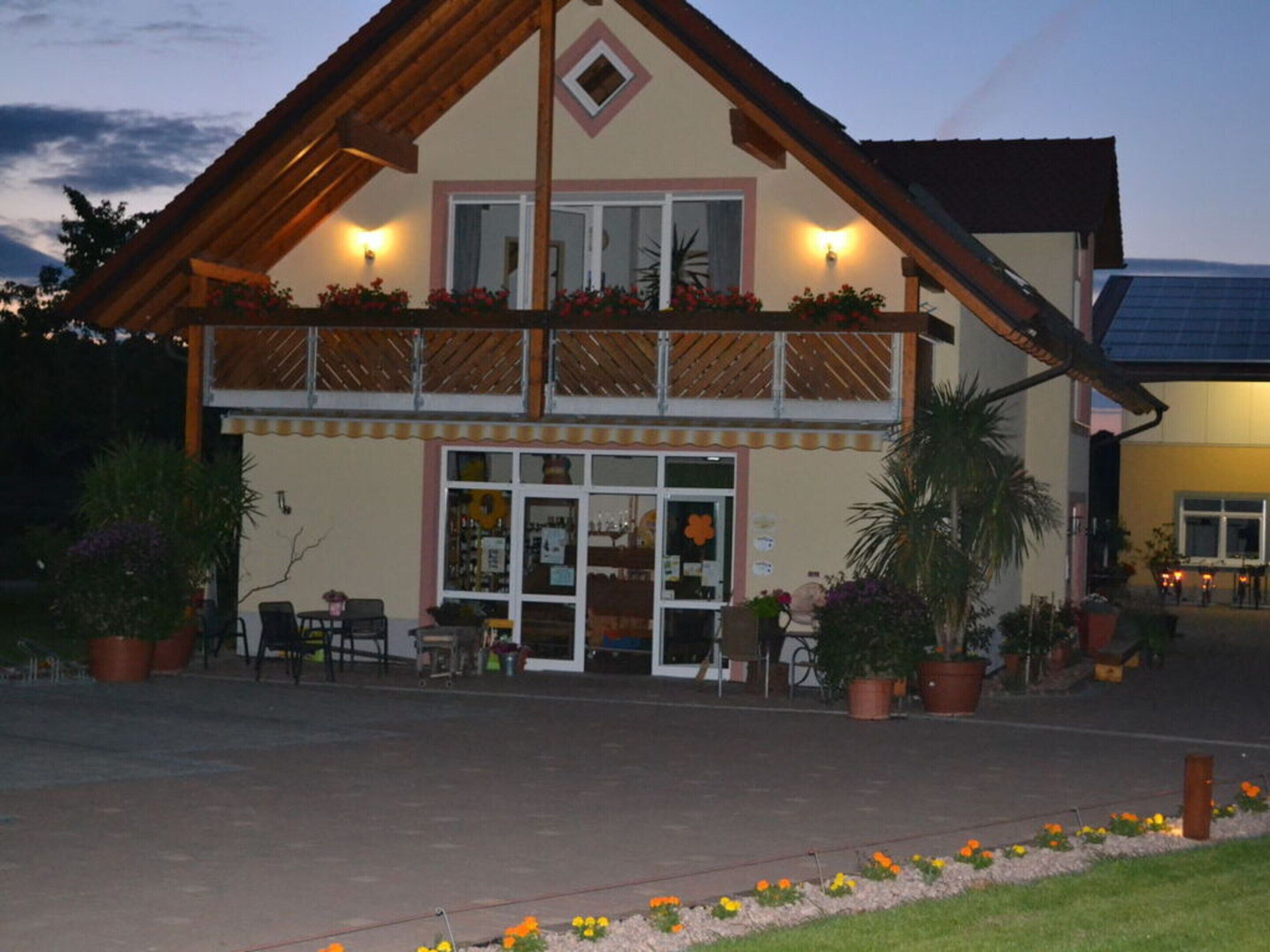 A two-story building with a balcony, outdoor seating, and potted plants.
