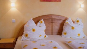 Ein Bett mit Holz-Kopfteil, zwei Kissen mit Sonnenblumenmuster und ein Herz-Gemälde an der Wand.