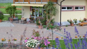 Ein zweistöckiges Haus mit Balkon, Außenbereich mit Sitzgelegenheiten und Topfpflanzen.