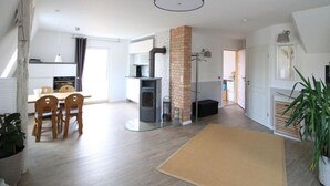 A modern kitchen with a built-in stove, a dining area with wooden chairs, and a large window providing natural light. - Holiday Apartment Mozartmansarde (Waren (Müritz))