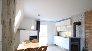 A modern kitchen with white cabinets, a wooden dining table, and a built-in wood stove. - Holiday Apartment Mozartmansarde (Waren (Müritz))