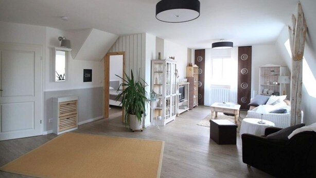 A spacious living area with a large window, a ceiling light, and a wooden floor. - Holiday Apartment Mozartmansarde (Waren (Müritz))