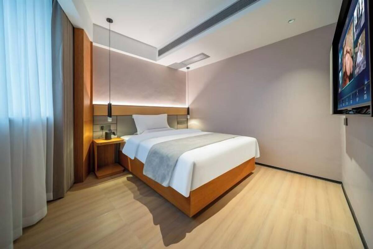 Quarto de hotel moderno com uma cama grande, mesa de cabeceira e televisão fixada na parede.