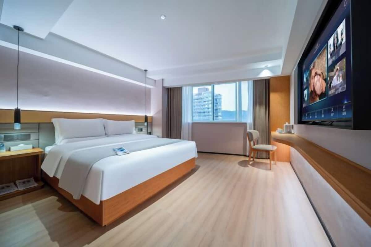 Quarto de hotel moderno com uma cama grande, televisão e vista para a cidade.