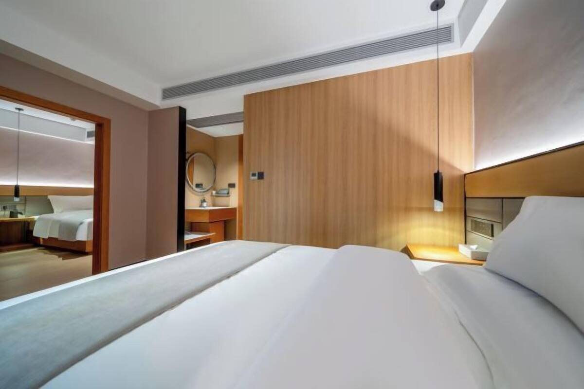Quarto de hotel com cama, mesa de cabeceira, espelho e parede de painéis de madeira.