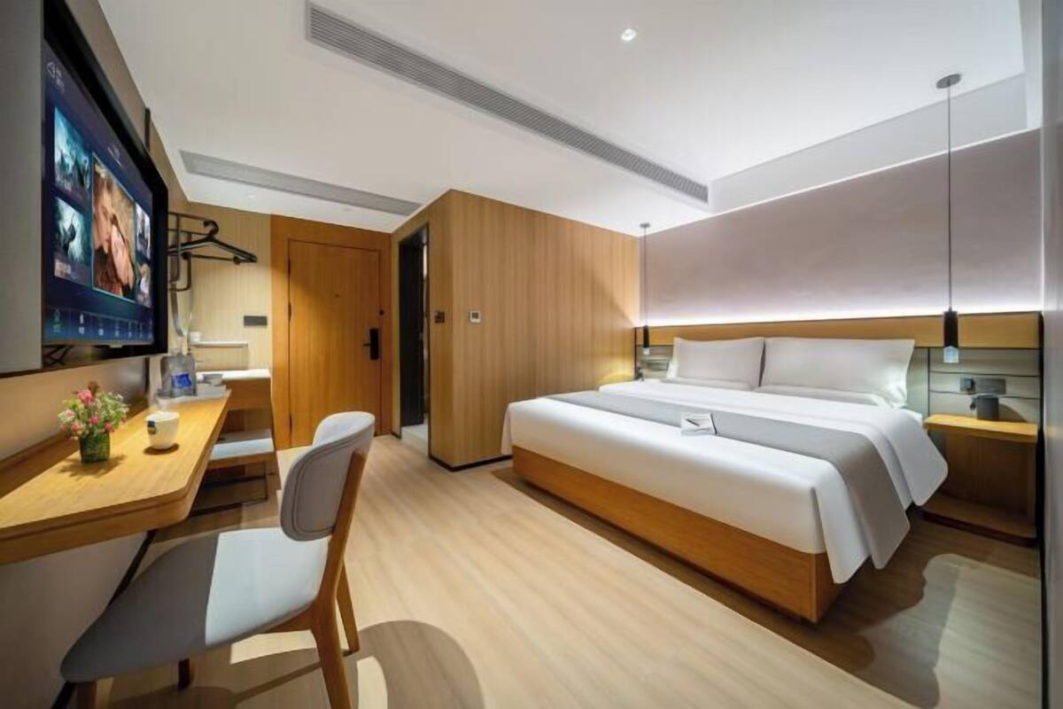 Quarto de hotel moderno com cama, escrivaninha, cadeira, televisão e painéis de madeira.
