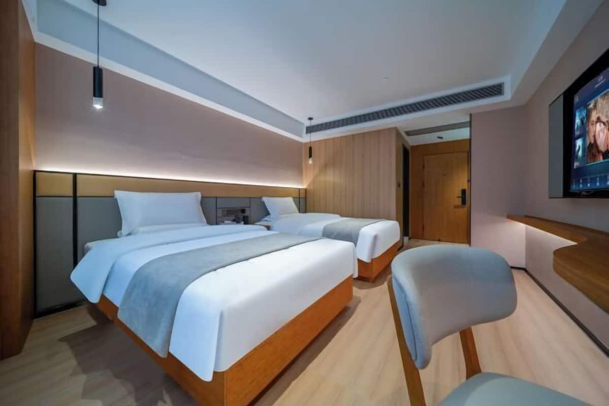 Quarto de hotel moderno com uma cama grande, uma cama menor, uma escrivaninha e uma televisão.