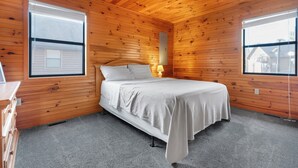Un dormitorio con paredes de madera, una cama, un ventilador de techo y dos ventanas.