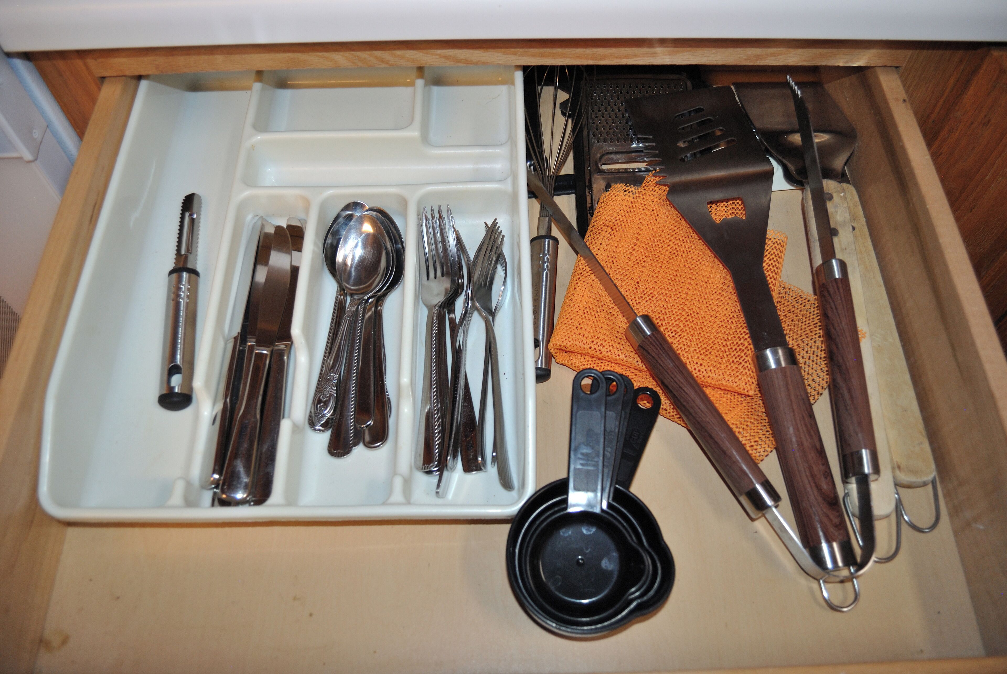 A drawer containing kitchen utensils and tools, including a spoon, forks, knives, and a grater.