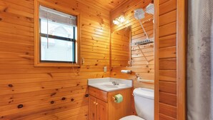 Baño de cabaña de madera con ventana, lavamanos, inodoro y ducha.