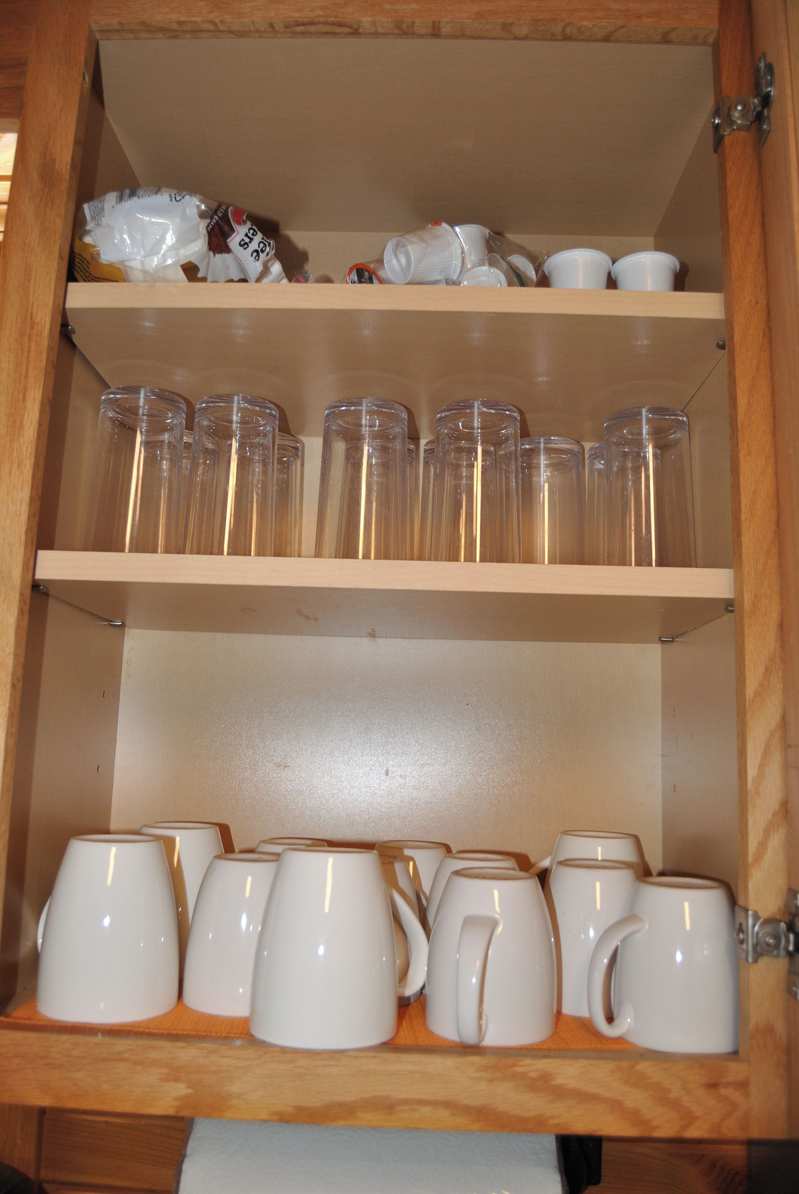 Ein Holzkabinent mit Regalen, auf denen klare Glasbecher, weiße Keramiktassen und eine Plastiktüte stehen.