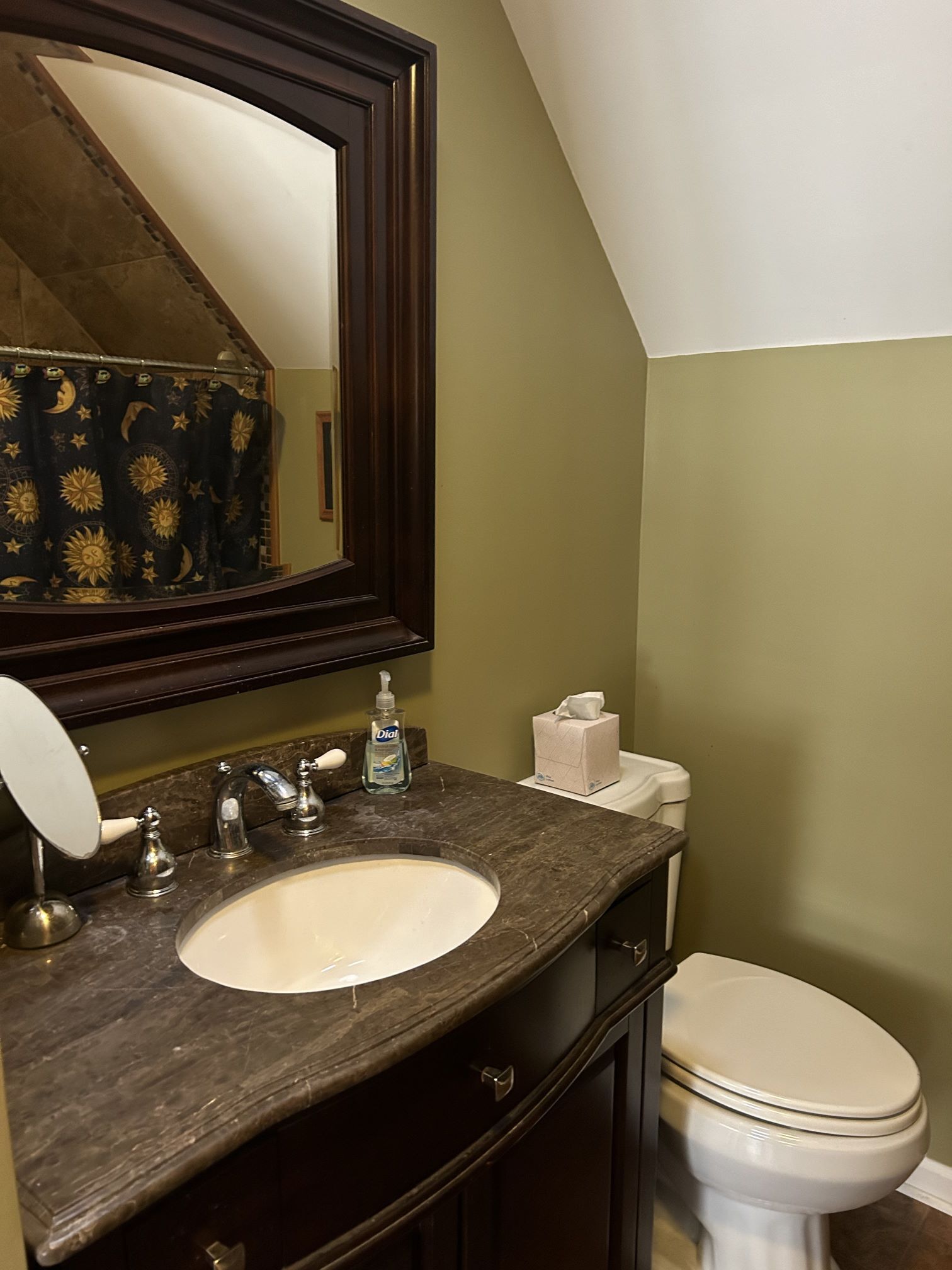 A bathroom with a dark marble sink, a large mirror, a toilet, and a shower curtain with a sun and moon pattern.
