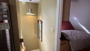 A compact kitchen with a refrigerator, a wooden staircase, a small rug, and a bed with a patterned bedspread in a bedroom. - Great Asheville Location (Asheville)