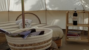 Ein Zeltraum mit einem Bett, einer kleinen Holzablage mit Büchern und einer Flasche sowie einem gewebten Korb.