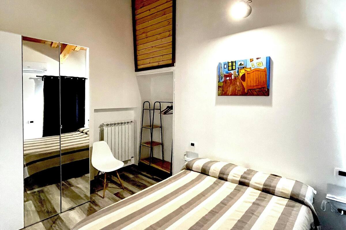 Un dormitorio con cama, una silla, un radiador, una escalera y un cuadro en la pared.